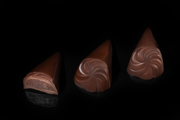 Chocolate candies on a dark background with reflection. Piece by piece and as a whole. Filling of nuts and fruits.