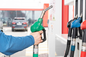 Man's hand picking up green handle of gas pump on gas station ready for refueling car. Gas or diesel refueling process. - obrazy, fototapety, plakaty