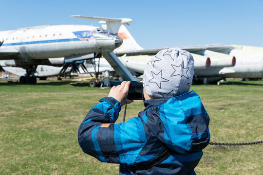 Boy with his camera is taking photos of old discommisioned airplanes, which stand outside in museum. Learning history of aviation.