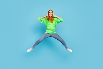 Fototapeta na wymiar Photo of pretty impressed young lady dressed green hoodie smiling jumping high isolated blue color background