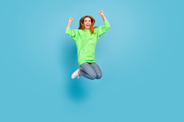 Photo of adorable lucky young lady dressed green hood smiling jumping high rising fists isolated blue color background