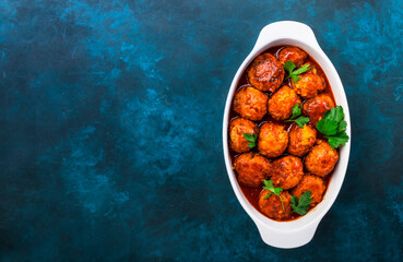 Meatballs with spicy tomato sauce in white baking dish on blue kitchen table. Top View
