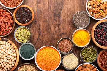 Superfoods, legumes, cereals, nuts, seeds set in bowls on wooden background. Superfood as chia, spirulina, beans, goji berries, quinoa, turmeric and other. Top view
