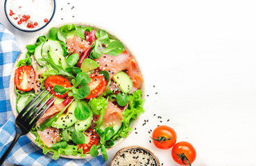 Fresh salmon salad with avocado, cucumber, sesame seeds, olive oil, tomatoes and mixed herbs. White background, top view