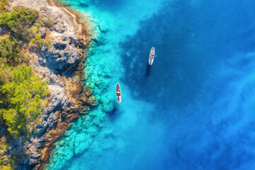 Aerial view of people on floating sup boards on blue sea, rocks, trees at sunset in summer. Blue...