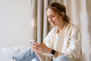 Young woman smiling while using cellphone in bedroom at home