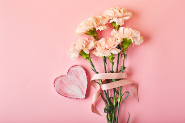 Bouquet of pink carnations and decorative heart. Design concept of holiday greeting with carnation bouquet on pink table background