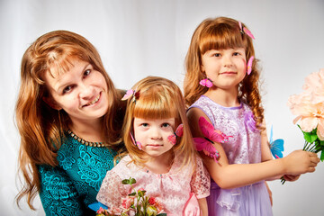 Cute daughters and mother with flowers in the studio on a white background. Young girls and woman posing indoors. Family during photo shoot in summer or spring time