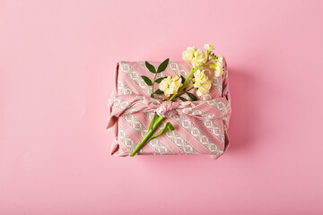 Bouquet of yellow matthiola with gift wrap in traditional japanese furoshiki style. Design concept of holiday greeting on pink table
