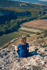 Young woman sits on a rock, looking at the landscape and enjoying the view and fresh air.