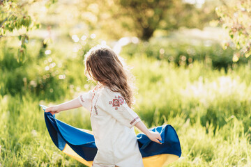 Ukrainian child girl in embroidered shirt vyshyvanka with yellow and blue flag of Ukraine in field.