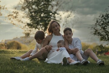 Mother and three children hugging. Happy family sitting outdoor: woman and two brother kids boys and cute little toddler boy