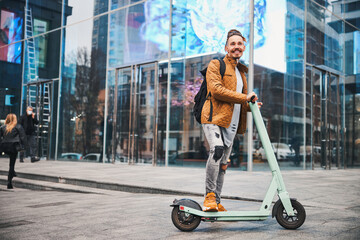 Happy owner of the modern scooter smiling cheerfully outdoors