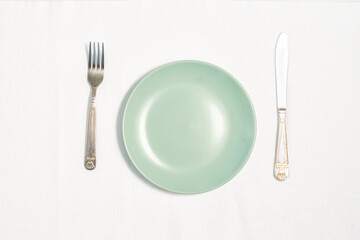 blue empty plate, knife and fork on white tablecloth