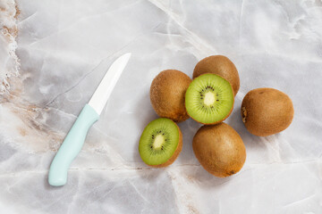 Whole and sliced kiwi fruits and knife on the kitchen table.
