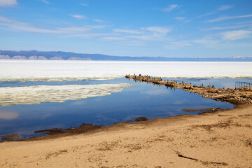 Sandy beach, old ruined wooden pier on the island of Olkhon in the spring. Lake Baikal during the ice drift.