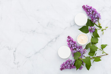 spring skin care, lilac on marble background. natural cosmetic product, set of cream mask in glass jar. beauty and wellness concept. copy space, text