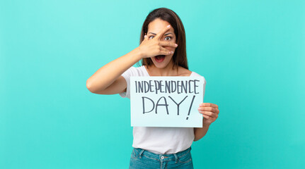 young hispanic woman looking shocked, scared or terrified, covering face with hand. independence...
