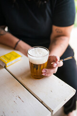 Mulher tomando cerveja em copo americano e segurando um cigarro de palha