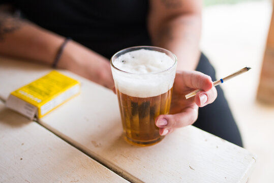 Mulher tomando cerveja em copo americano e segurando um cigarro de palha