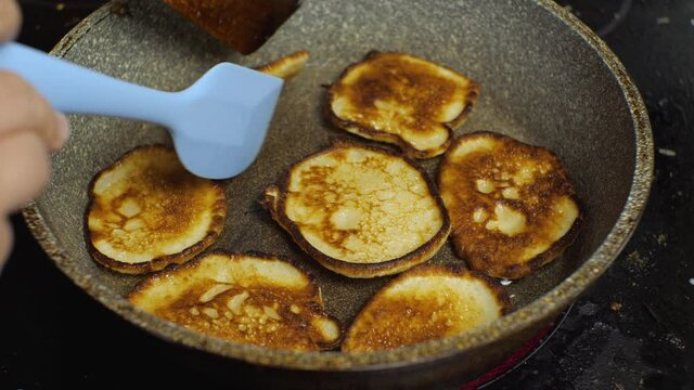 Using the spatulas, check the readiness of the pancakes in the pan. The process of making pancakes in the home kitchen close-up