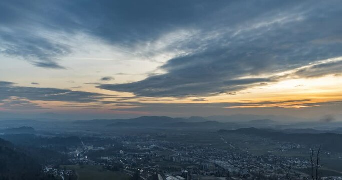 Time lapse of colorful sunset over small town Kamnik, Slovenia. Elevated view of colorful clouds and urban area in Europe. Mountains and hills in the distance. Wide angle, zoom in