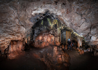 A beautiful cavern full of stalactite and stalagmite formations. Speleology in a cave. The silhouette of a man illuminating the formations of a cave. Grotto inside the earth