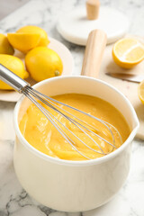 Delicious lemon curd and whisk on white marble table