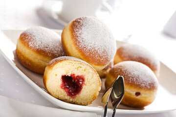 Bismarck doughnuts filled with jam and decorated with confectioner's sugar on a platter with pastry tongs - obrazy, fototapety, plakaty