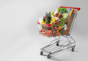 Shopping cart full of groceries on grey background. Space for text - obrazy, fototapety, plakaty