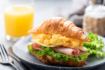 Croissant sandwich with ham, cheese, scrambled eggs for breakfast served with glass of orange juice