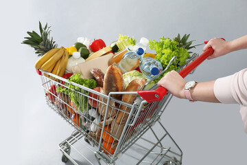 Woman with shopping cart full of groceries on grey background, closeup © New Africa