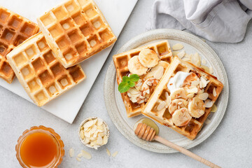 Breakfast belgian waffles with banana, yogurt and almonds, table top view. Sweet dessert waffles - 435832432