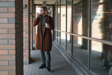 Young businessman talking on mobile phone and drinking coffee while standing in the city