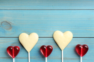 Heart shaped lollipops made of chocolate and sugar syrup on turquoise wooden table, flat lay. Space for text