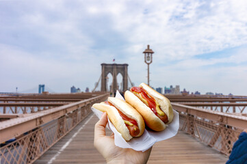 Holding two hot dogs in NYC on the Brooklyn Bridge