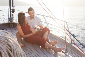 Couple in love drinking wine on yacht by sea. Happy travelers relaxing, traveling and enjoying summer vacation