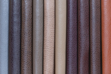 Colored leather for furniture upholstery in brown and beige shades. Samples of fabric for furniture of different shades, folded in stripes close-up.