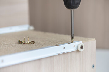 Screwing the roller guide to the bottom of the box. Do-it-yourself furniture assembly at home using a screwdriver and a bunch of screws.