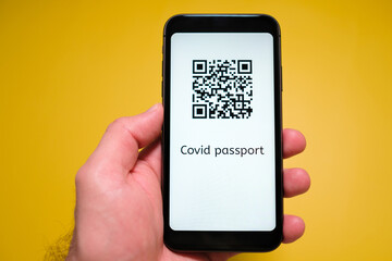 A smartphone with electronic immune digital health passport, Covid pass with QR code in mans hand on the yellow background.