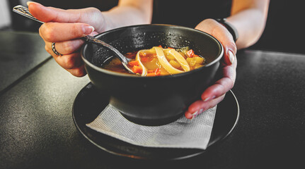 Woman hand eating chicken soup in black bowl sitting in cafe