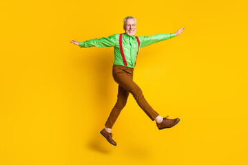 Fototapeta na wymiar Full length profile side photo of senior man happy positive smile go walk jump hands wings plane fly isolated over yellow color background