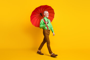Full size profile side photo of aged man happy positive smile go walk wet rain parasol isolated over yellow color background © deagreez