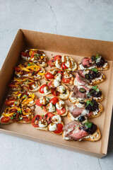 
A set of different snacks for a party or a festive table. Ciabatta sandwiches with tomatoes, jamon, cream cheese, vegetables, chambers and olives. Delicious wine snacks