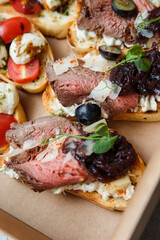 
A set of different snacks for a party or a festive table. Ciabatta sandwiches with tomatoes, jamon, cream cheese, vegetables, chambers and olives. Delicious wine snacks