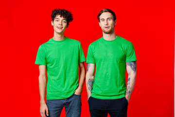 joyful friends in green t-shirts are standing next to red background