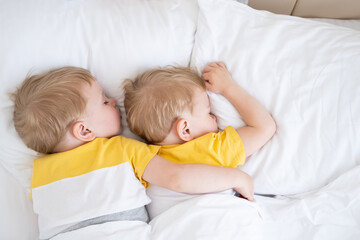 two blonde boys twins sleeping hugging on white bedding - obrazy, fototapety, plakaty