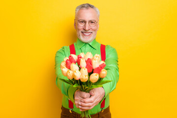 Photo of aged man happy positive smile give present flowers celebration isolated over yellow color background