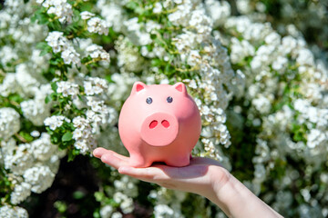 Girl holding piggy Bank against the background of blossoming cherry
