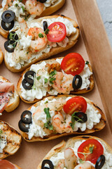 
A set of different snacks for a party or a festive table. Ciabatta sandwiches with tomatoes, jamon, cream cheese, vegetables, chambers and olives. Delicious wine snacks